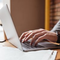 Cropped image of business man sitting by the table in cafe and using laptop computer